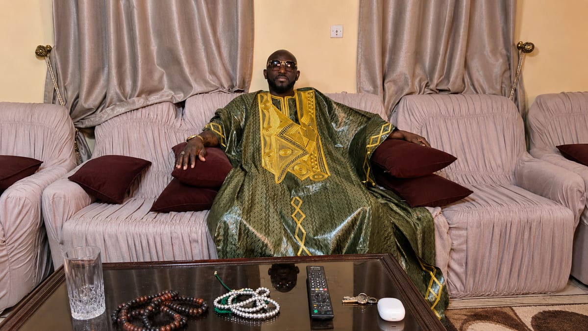 Marabout Djibril con bubú verde y oro, con los rosarios delante